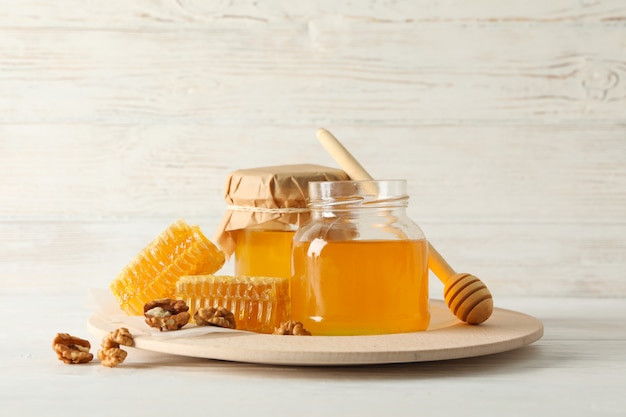 Honeycombs, walnuts, dipper and jars with honey on wooden background