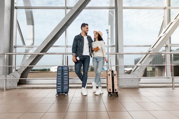 ハネムーンは空港でスーツケースを持って立っているロマンチックな若いアラブのカップルを旅行します