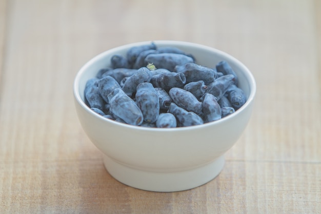 Жимолость синяя ягода (Honeyberries, woodbine, woodbind) на белой тарелке на деревянном столе