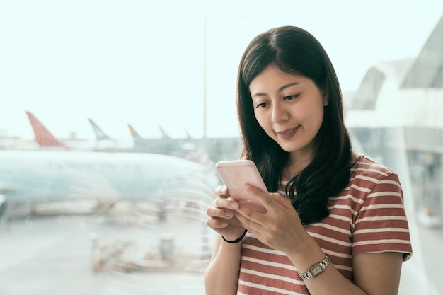 香港空港電話旅行ビジネス クラスのラウンジでモバイル スマート フォンを使用して飛行機のフライトのテキスト メッセージの sms メッセージを待っているアジア交換留学生。技術と旅行の人々 VIP ライフ スタイル