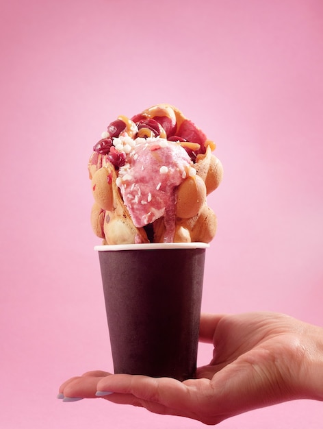 Hong Kong waffles in cup in hand on pink background