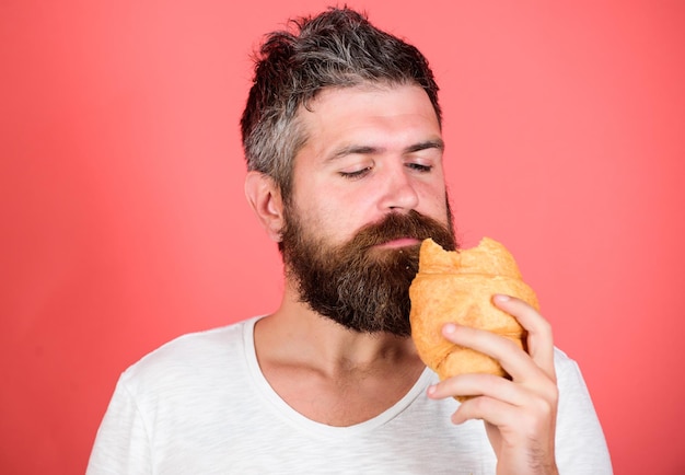 Hongerige hipster bite croissant Heerlijk ontbijt Ongezond maar lekker ontbijt Perfecte match voel honger Bebaarde hipster geniet van ontbijt Ochtendtraditie concept Vers gebakken croissant