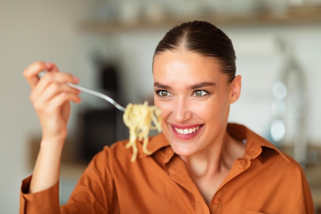 Hongerige jonge blanke vrouw die smakelijke zelfgemaakte pasta eet en naar spies spaghetti kijkt