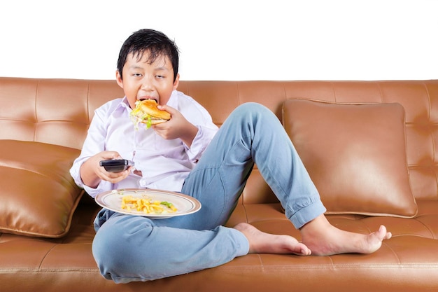 Hongerige jongen die hamburger eet terwijl hij tv kijkt