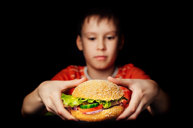 Hongerige jongensholding mond-water gevende hamburger die op dark wordt geïsoleerd