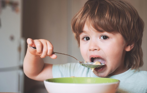 Hongerige kleine jongen die een vrolijk babykind eet, eet zelf voedsel met een lepel, lekker kinderontbijt, baby e