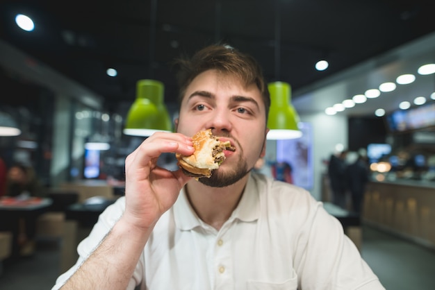 hongerige man geniet van een heerlijke burger in een fastfoodrestaurant.