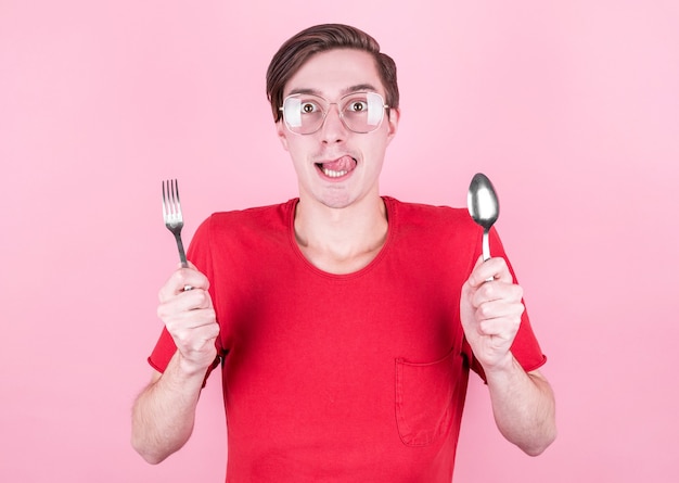 Hongerige man houdt een vork en lepel in zijn handen en denkt over heerlijk eten over roze muur. Dieet en maaltijdconcept.