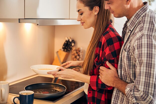 Hongerige man kijkt toe hoe haar vrouw een omelet maakt