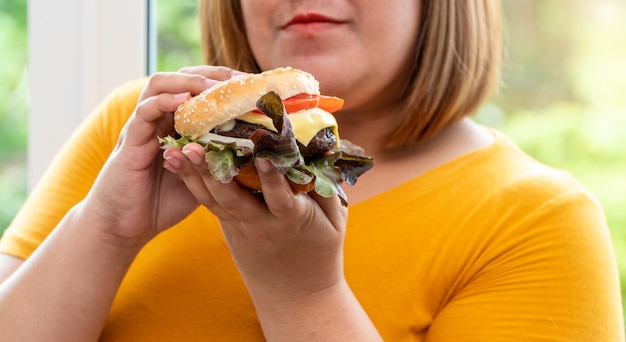 Hongerige overgewicht jonge Aziatische vrouw met hamburger, haar altijd hongerig en te veel eten, gulzigheid en eetbuien.