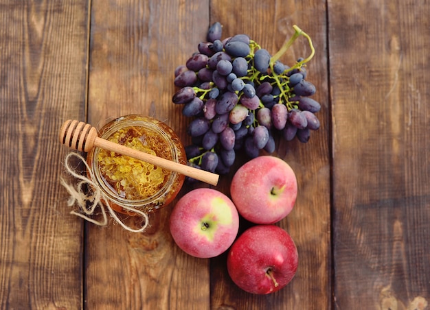 Honing in een mooie pot, houten lepel spindle, druiven en appels op een houten achtergrond