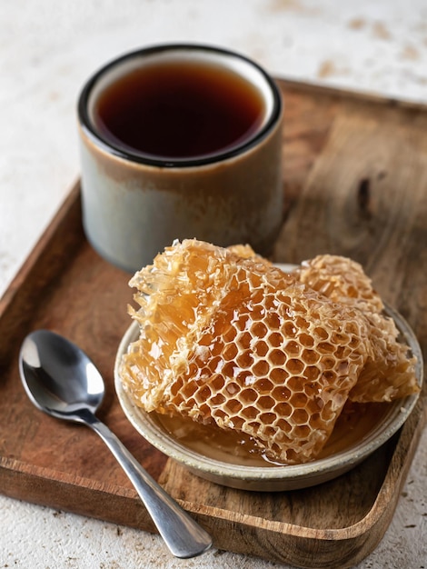 Honing in honingraten in een schotel met thee en lepel op houten dienblad Kopieer de ruimte