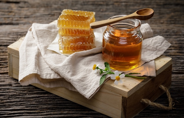Honingbij in kruik en honingraat met honingsdipper en bloem op houten lijst