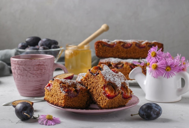 Honingtaart met pruimen bestrooid met poedersuiker een potje honing en een kopje koffie