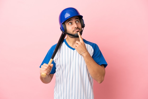 Honkbalspeler met helm en vleermuis geïsoleerd op roze achtergrond met twijfels tijdens het opzoeken