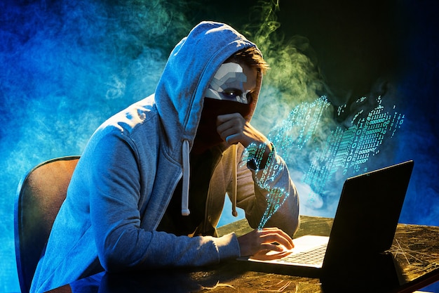 Hooded computer hacker stealing information with laptop. Concept of threat