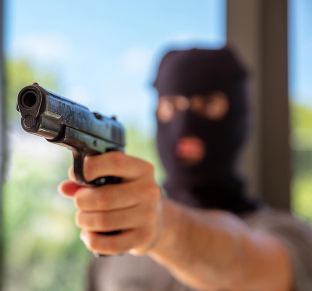 Hooded robber hand holding a pistol blur background