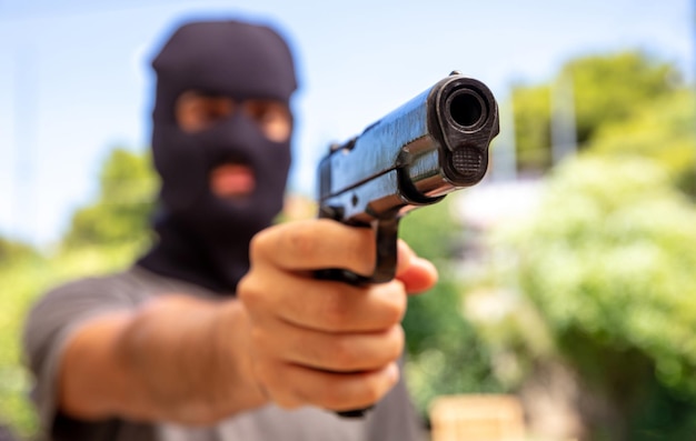 Hooded robber hand holding a pistol blur background