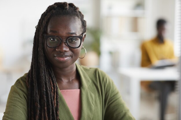 Hoofd en schouders portret van jonge Afro-Amerikaanse vrouw camera kijken en glimlachen terwijl u geniet van het werk op kantoor, kopieer ruimte