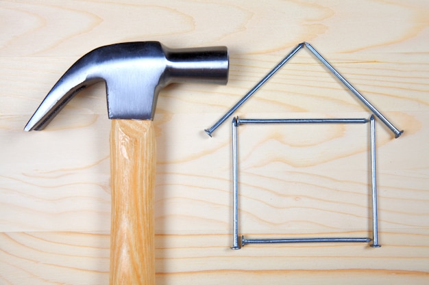 Hoofd van hamer en huis van spijkers op houten achtergrond