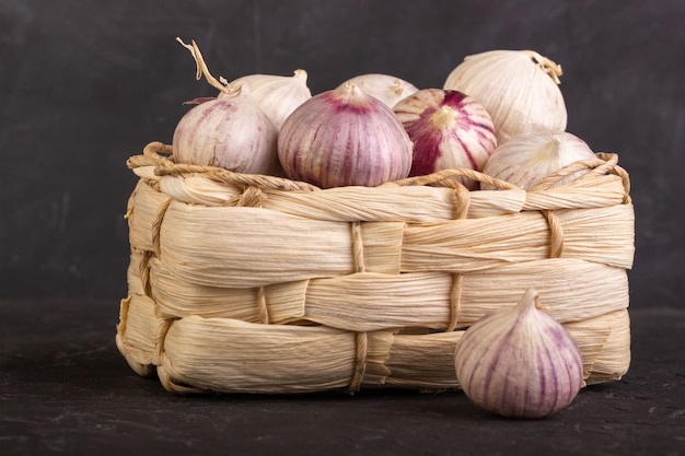 Foto hoofden van knoflook in een rieten mand op een donkere achtergrond