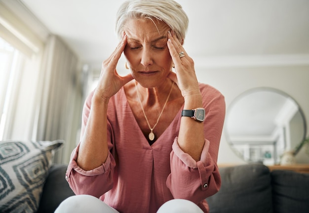 Hoofdpijn pijn angst en senior vrouw denken aan psychische problemen op de bank in de woonkamer in huis Trieste bejaarde met depressie thuis stress en gefrustreerd met pensioen op de bank