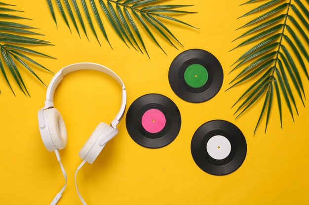 Hoofdtelefoons en vinylplaten palmgroene bladeren op gele achtergrond Muziekconcept Tropische compositie Bovenaanzicht Plat leggen