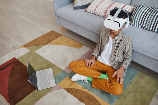 Hoog hoekportret van een Afro-Amerikaanse tienerjongen die VR-uitrusting draagt tijdens het spelen van videogames die thuis op de vloer zitten, kopieer ruimte