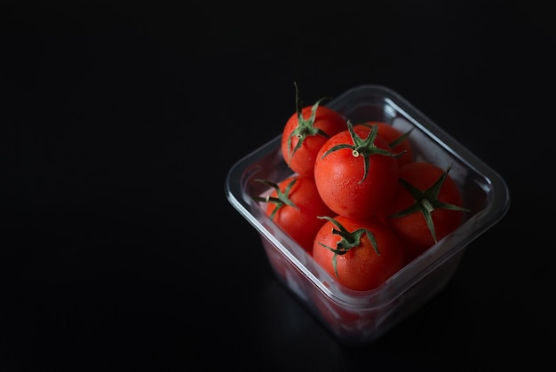 Foto hooghoek close-up van kersentomaten in een container tegen een zwarte achtergrond