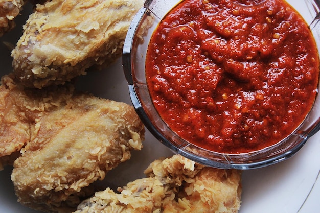 Hooghoek uitzicht op gebakken kip en rode chili saus plaat op tafel