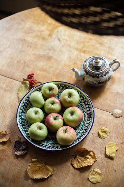 Foto hooghoekbeeld van appels op een bord met droge bladeren op een houten tafel