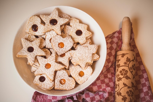 Foto hooghoekbeeld van de schaal met linzerkoekjes tegen een tafeldoek en een deegroller