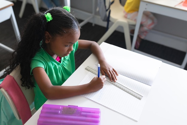 Hooghoekbeeld van een Afrikaans-Amerikaans basisschoolmeisje dat op een boek schrijft in het klaslokaal