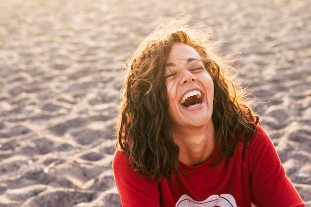 Hooghoekbeeld van een gelukkige jonge vrouw die lacht terwijl ze op het strand zit