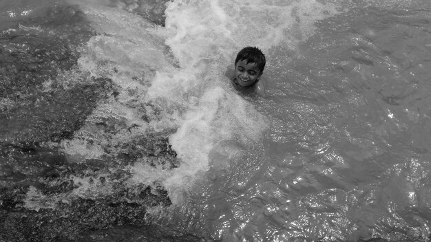 Foto hooghoekbeeld van een glimlachende jongen die in de zee zwemt