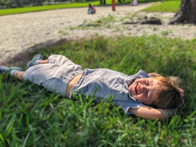 Foto hooghoekbeeld van een jongen die op het gras op de speeltuin ligt