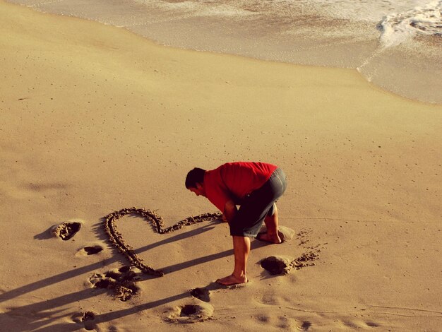 Foto hooghoekbeeld van een man die een hartvorm maakt op het zand op het strand