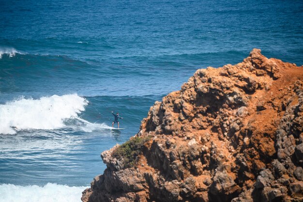 Foto hooghoekbeeld van een man die in zee surft bij rotsen