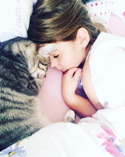 Hooghoekbeeld van een meisje dat thuis met een kat op het bed slaapt