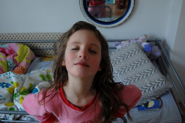 Foto hooghoekbeeld van een meisje met gesloten ogen dat op het bed zit