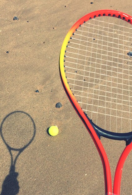 Foto hooghoekbeeld van een tennisracket en een bal op zand