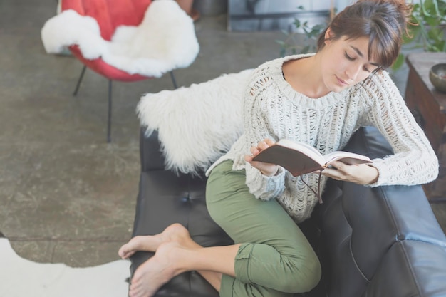 Foto hooghoekbeeld van een vrouw die een boek leest terwijl ze thuis op de bank zit