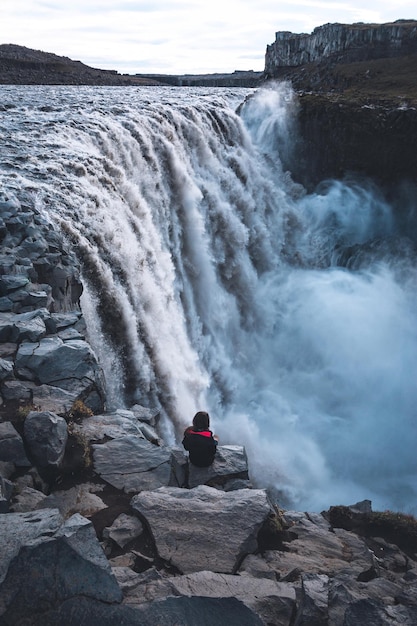 Hooghoekbeeld van een vrouw die op een rots bij een waterval zit