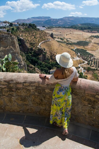 Foto hooghoekbeeld van een vrouw met een hoed die bij de muur tegen het landschap staat