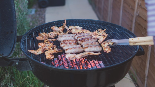 Hooghoekbeeld van kippenvleugels en worstjes op barbecue grill