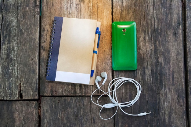 Foto hooghoekbeeld van mobiele telefoon met dagboek en in-ear koptelefoon op tafel