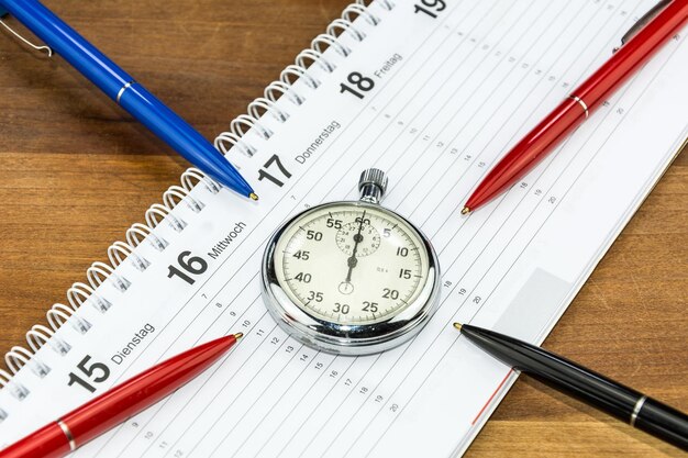 Foto hooghoekbeeld van pennen met stopwatch en kalender op tafel