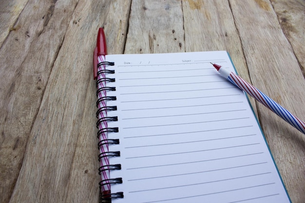 Hooghoekbeeld van spiraalvormige notebook en pennen op een houten tafel