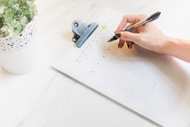 Hooghoekbeeld van vrouw met pen over kalender op tafel