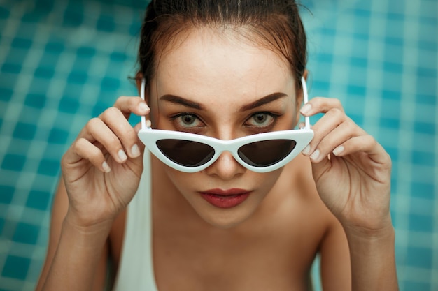Hooghoekportret van een jonge vrouw met een zonnebril in een zwembad